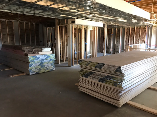Interior view of a basement under construction, featuring stacked drywall and insulation materials, showcasing the renovation process by Basements & Bars.